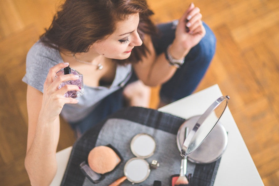 Woman sitting  with makeup, applying perfume while looking in the mirror. Mia's aromatherapy roll-ons and perfume, nature in a bottle. Photo courtesy of Pexels.