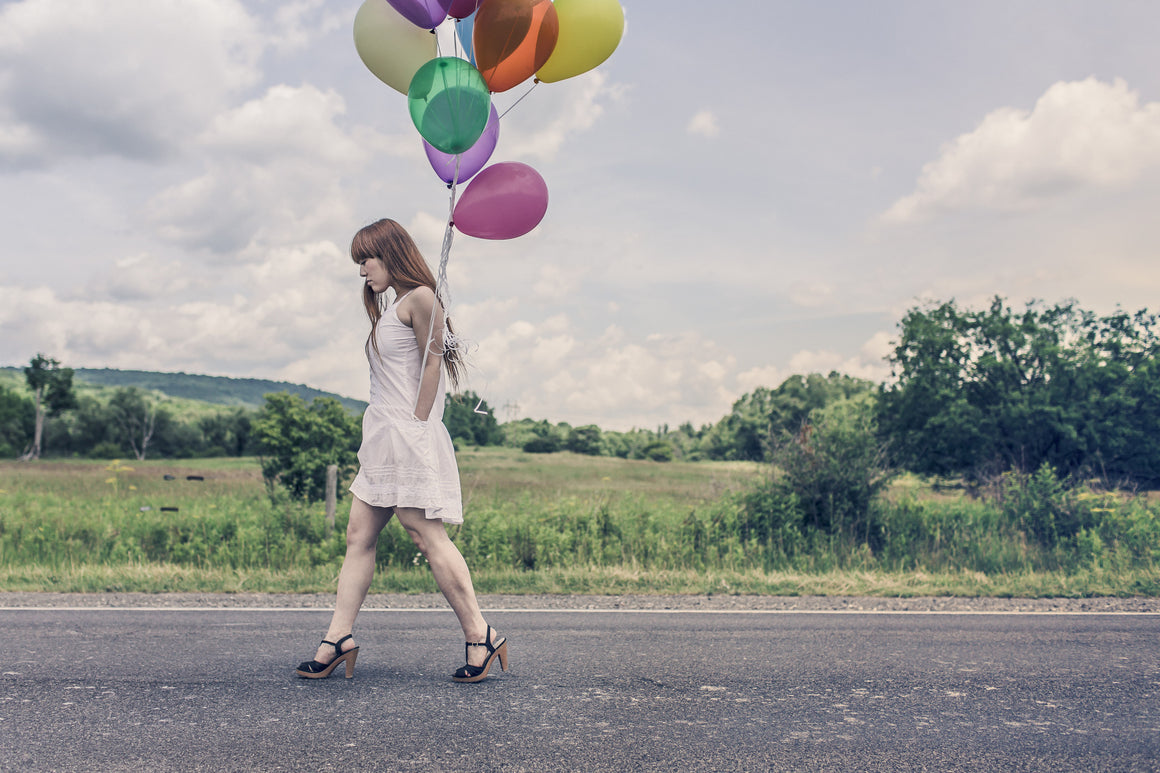 Woman walking down street in the country with balloon's in her hand. Give the gift of nature with Mia's Aromatherapy. Photo courtesy of Pexels.