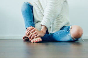 Woman sitting on the floor with hand on her feet. Restore and protect using Mia's aromatherapy products. Photo courtesy of StockSnap.